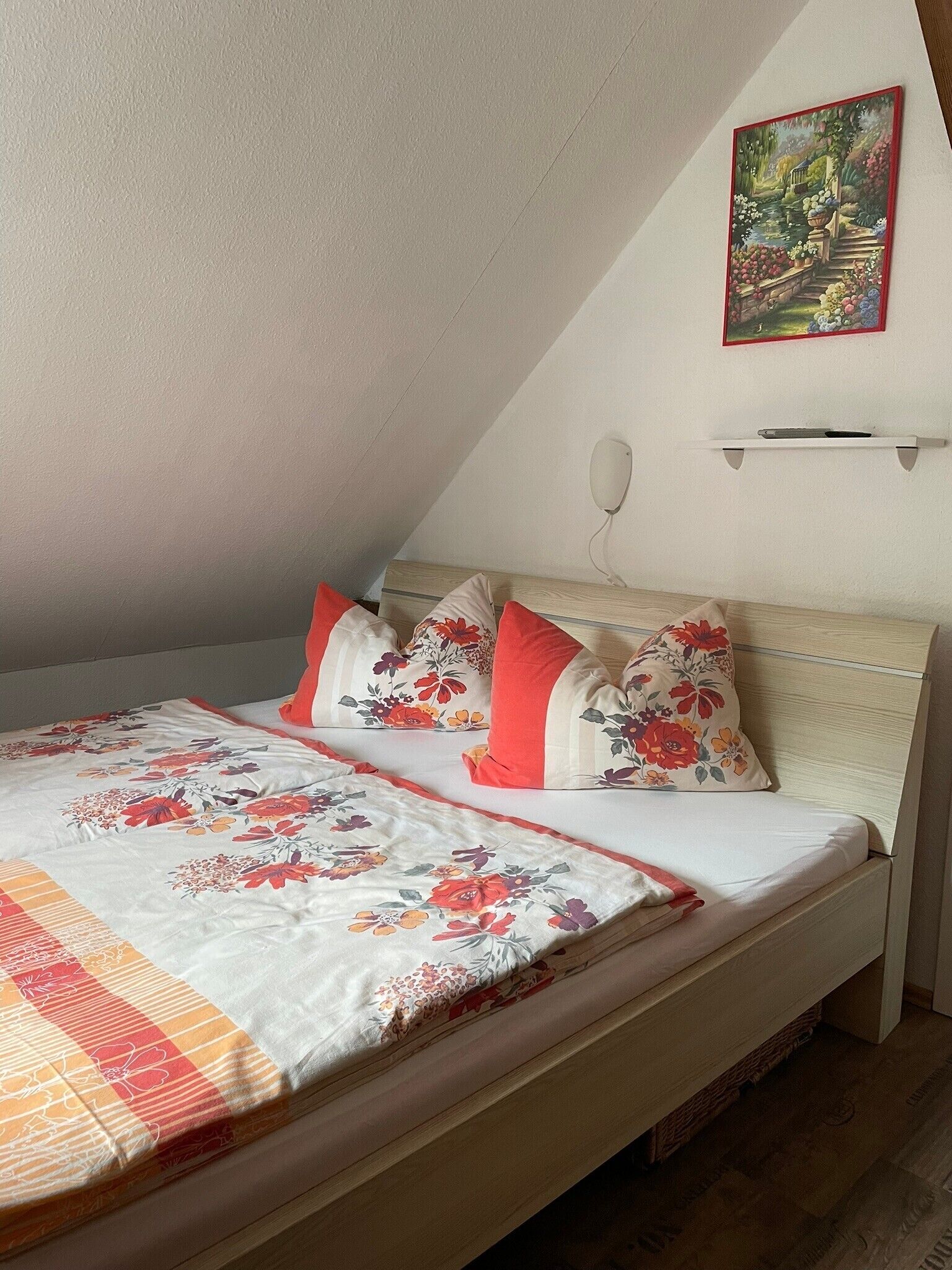 A bedroom with a bed, pillows, a painting, and a shelf.