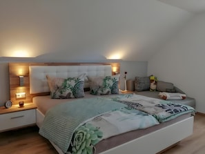 Quarto moderno com cama grande, mesas de cabeceira, um criado-mudo e uma luminária fixada na parede.