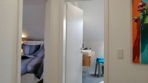 A hallway leading to a bedroom with a bed and a bathroom with a sink and a chair.