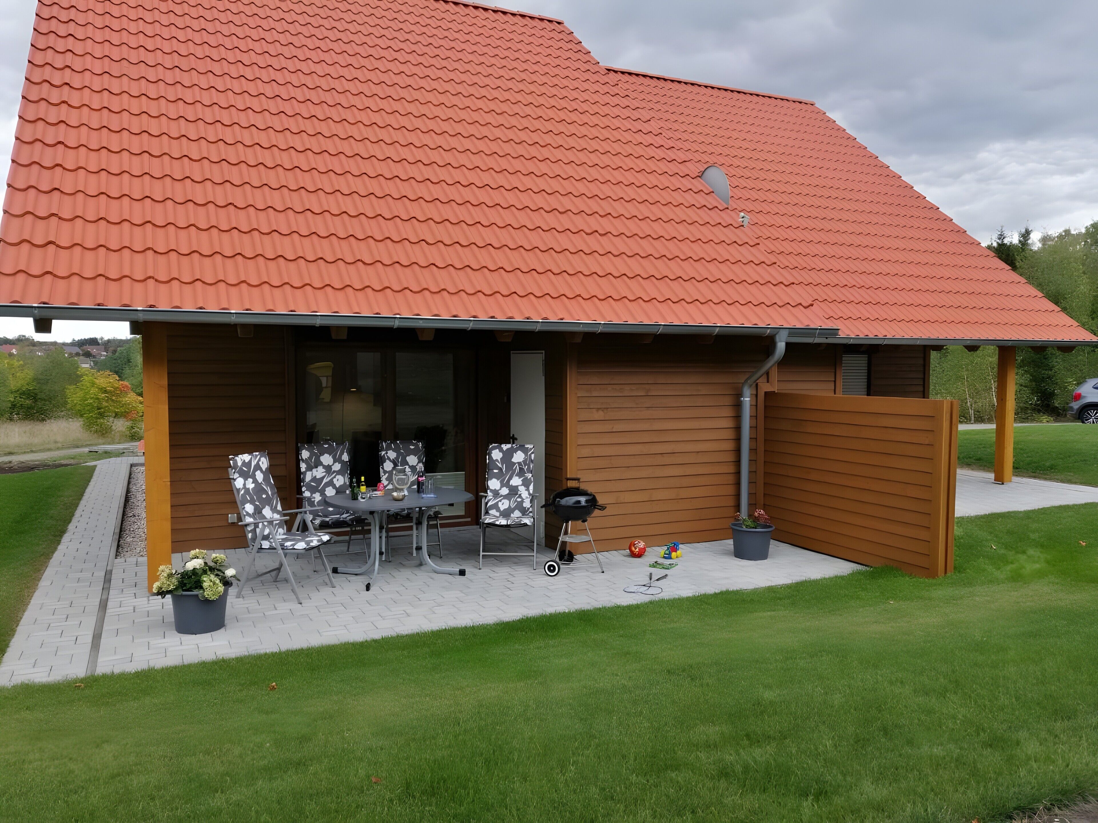A house with a red tiled roof, a covered patio with a table and chairs, and a fenced yard.