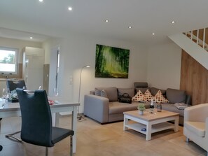 A modern living room with a dining area, a staircase, and a painting of a forest. - Holiday Home 'Hexenpfad' with Private Terrace, Private Garden and Wi-Fi (Hasselfelde)