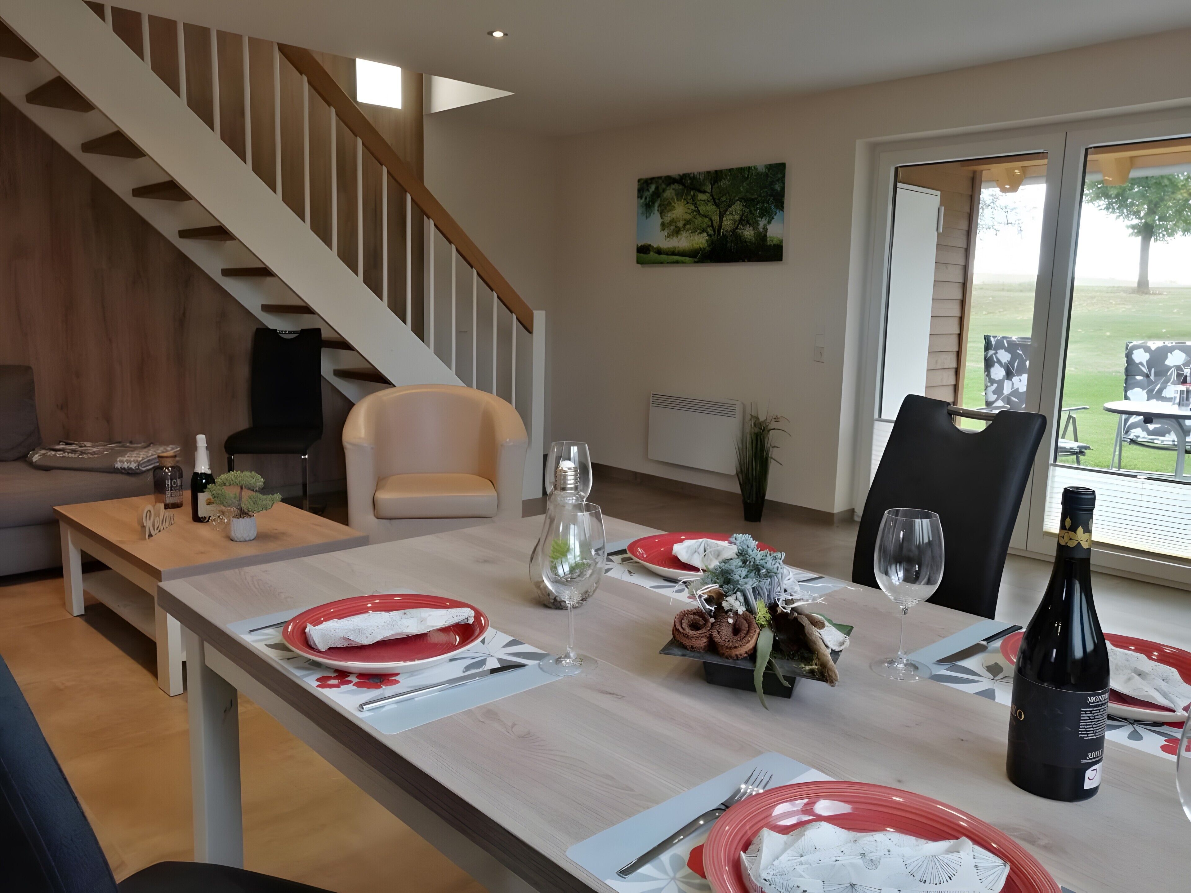 A dining area with a table set for two, a bottle of wine, and a painting on the wall.