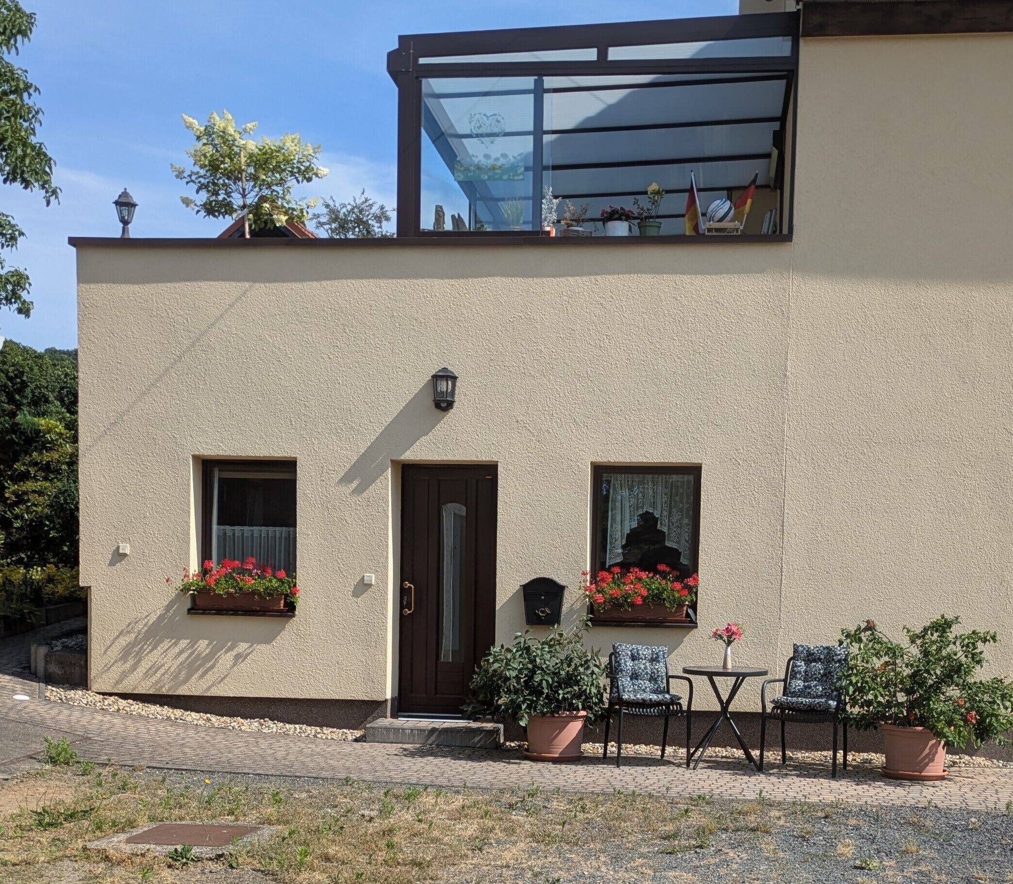 A two-story building with a beige exterior, a dark brown door, and windows with flower boxes. There are outdoor seating arrangements with chairs and a table.