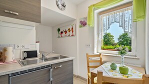 Una cocina moderna con un lavamanos, encimera y armarios. Hay una mesa de comedor con sillas y una ventana con vistas a la vegetación.