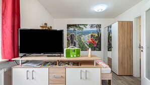 Una habitación con televisión, radio y carteles en un escritorio, un armario y una puerta.