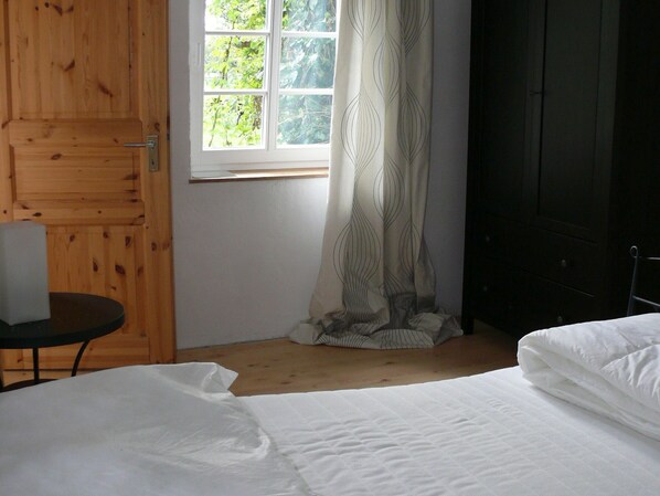 A bedroom with a bed, a wooden door, a window with curtains, and a small table.