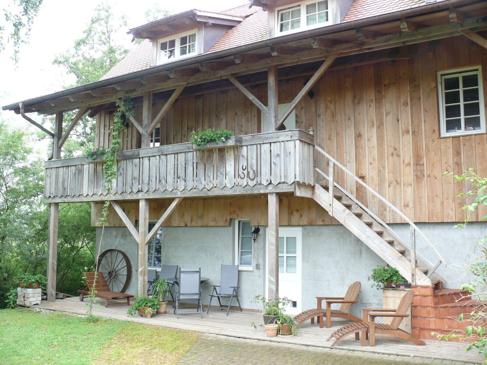 A wooden house with a balcony, outdoor seating, and a large wheel.