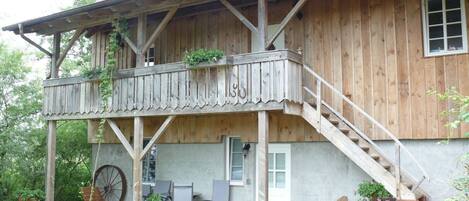 A wooden house with a balcony, outdoor seating, and a large wheel.