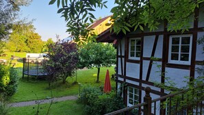 Uma casa tradicional em enxaimel com um jardim, um trampolim e uma RV branca ao fundo.