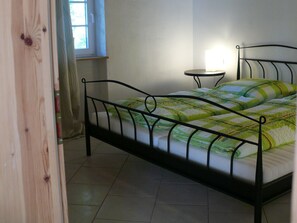 Een eenpersoonsbed met metalen frame, een nachtkastje en een raam met gordijnen.