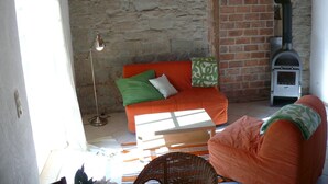 Une pièce chaleureuse avec un mur en pierre, une cheminée en briques, un canapé et un fauteuil en osier.