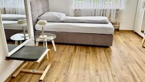 Un dormitorio minimalista con una cama, una mesita redonda pequeña, una silla y un espejo.