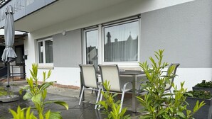 Un patio con mesa y sillas, una ventana con cortinas y plantas en macetas.