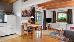 Una habitación acogedora con una mesa de comedor de madera, sillas, un televisor, un sofá y una ventana con cortinas.