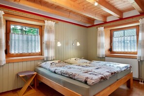 Ein Schlafzimmer mit einem hölzernen Bett, zwei mit Vorhängen versehenen Fenstern, einer Bank und Wandleuchten.