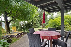 Eine überdachte Terrasse mit Tisch und Stühlen, umgeben von Grünpflanzen und einem Baum.