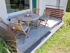 Un patio al aire libre con una mesa redonda, dos sillas de madera y un banco.