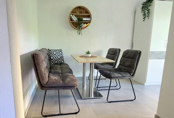 Una habitación moderna con sofá, dos sillones, una mesita, estantería y planta colgante.