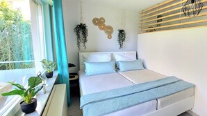 Een slaapkamer met een bed, een raam met gordijnen, een kamerplant en decoratieve wandaccessoires.