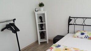 A bedroom with a bed, a clothing rack, a shelf with a plant, and a small black box. - Apartment 'Am Finkenweg Ground Floor' with Shared Terrace and Wi-Fi (Bestwig)