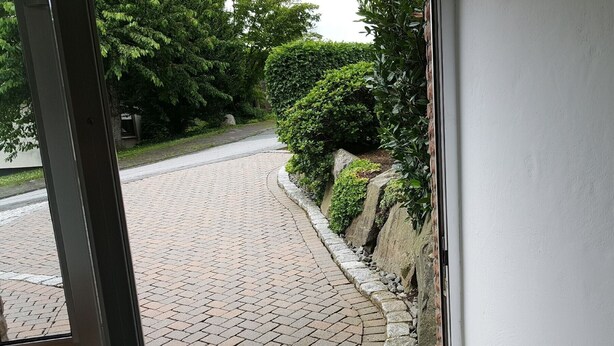 A paved driveway leading to a building entrance, surrounded by greenery and stone walls. - Apartment 'Am Finkenweg Ground Floor' with Shared Terrace and Wi-Fi (Bestwig)