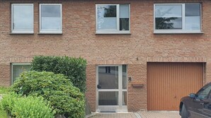 A two-story brick building with a garage door, a small front garden, and a parked car.