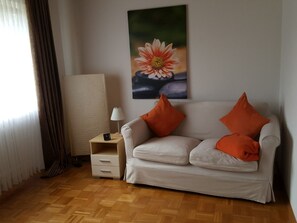 Una habitación con sofá, lámpara, reloj y un cuadro de una flor en la pared.