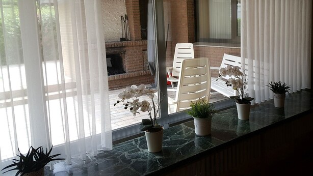 A room with a view of a brick fireplace, white chairs, and potted plants on a marble countertop.