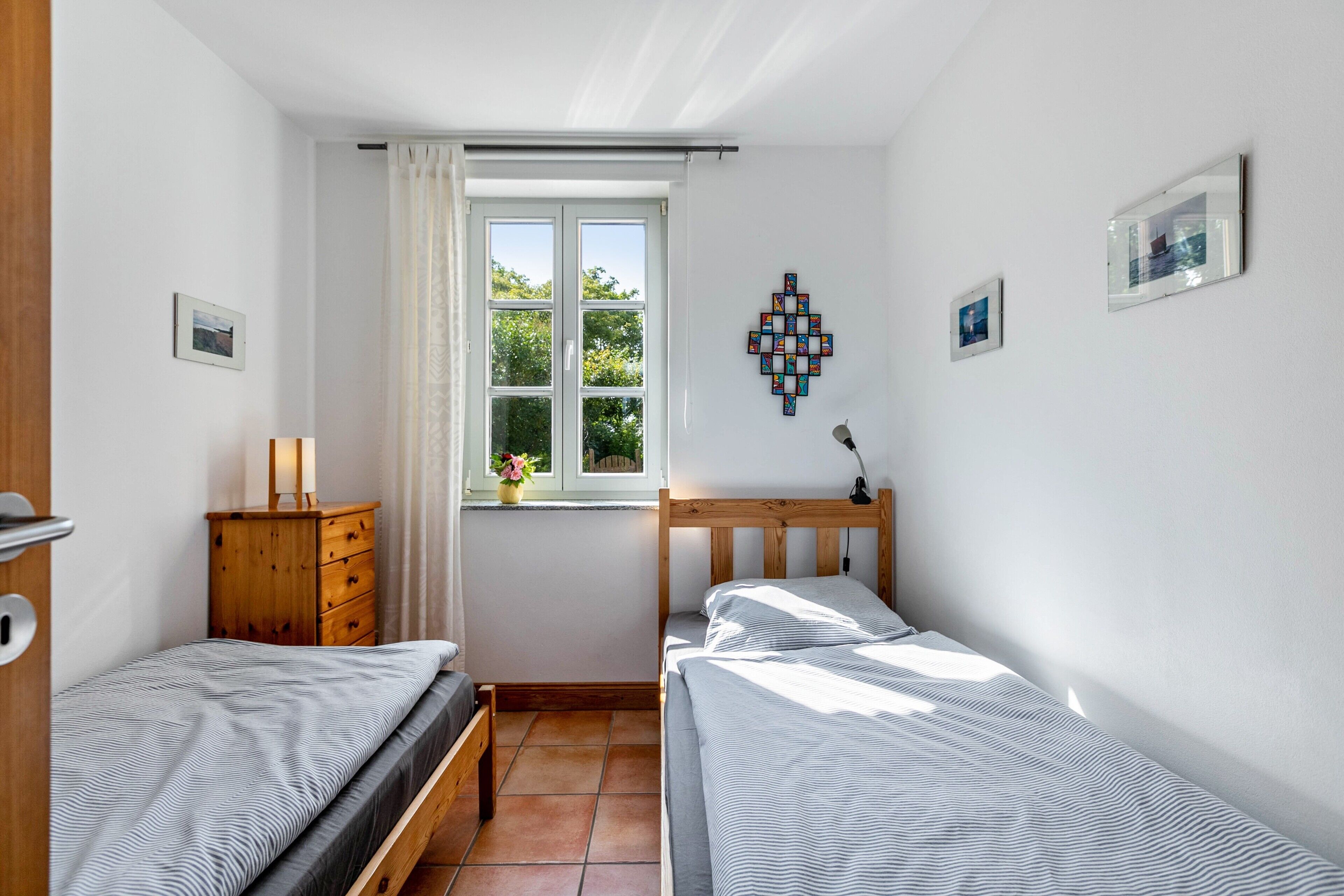 Ein Schlafzimmer mit zwei Betten, einer Holzkommode, einem Fenster mit Vorhängen und Bildern an der Wand.