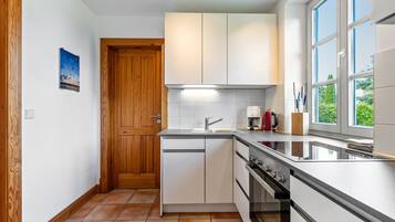 Una cocina compacta con armarios blancos, horno empotrado y ventana con vistas a zonas verdes.