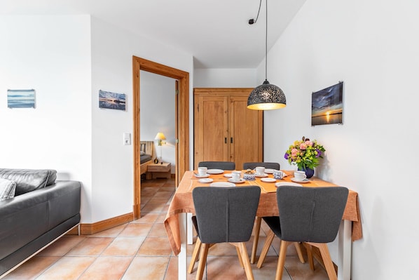 Un coin repas avec une table dressée pour quatre personnes, un canapé, un meuble en bois et une suspension.