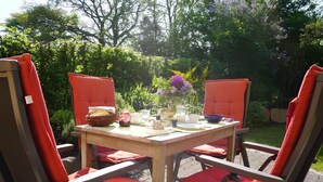 Une table en bois, entourée de chaises rouges, de verdure et d’un bassin.