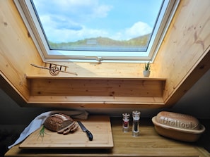A skylight with a wooden bench, a loaf of bread, a knife, two salt shakers, and a small potted plant.