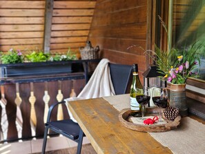 A wooden table with a bottle of wine, two glasses, a vase with flowers, and a pine cone on a tray.