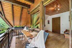 Un intérieur en bois avec un balcon, une table à manger avec des chaises, un lit et une porte en bois.