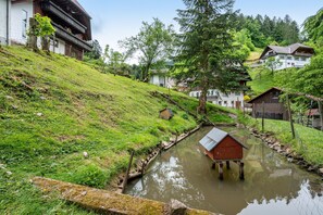 Un village rural avec des maisons construites sur une colline, un petit ruisseau et une structure en bois au milieu de l’eau.