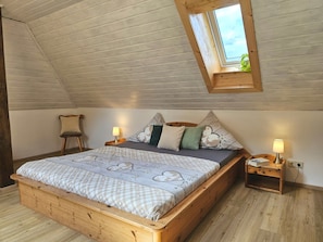 A bedroom with a sloped ceiling, a skylight, a wooden bed, two bedside tables, and a nightstand.