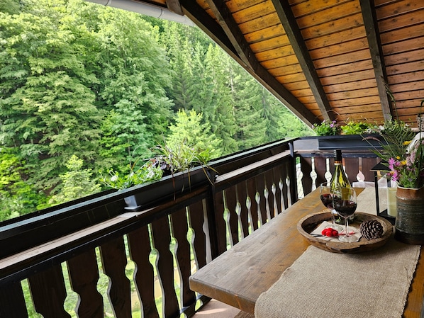 A balcony with a wooden railing, a table with a bottle of wine, glasses, and a pine cone.