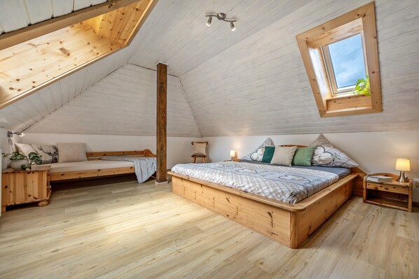 Une chambre à coucher de style « loft », avec un plafond en pente en bois, un lit intégré, un petit coin salon et une lucarne.