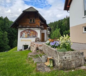 A traditional wooden building with a mural, a stone wall with flowers, and a grassy area.