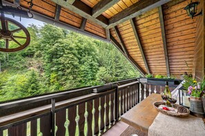Ein Holzbalkon mit Blick auf einen Wald, ein Tisch mit Flasche und Glas sowie eine Laterne.