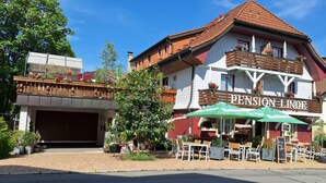 Rakennuksessa on kyltti, jossa lukee »Pension Linz», ja sen ulkopuolella on terassialue, jossa on aurinkovarjoja.