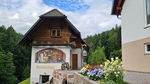 Ein traditionelles Holzgebäude mit Wandgemälde, eine Steinmauer mit Blumen und eine Rasenfläche.