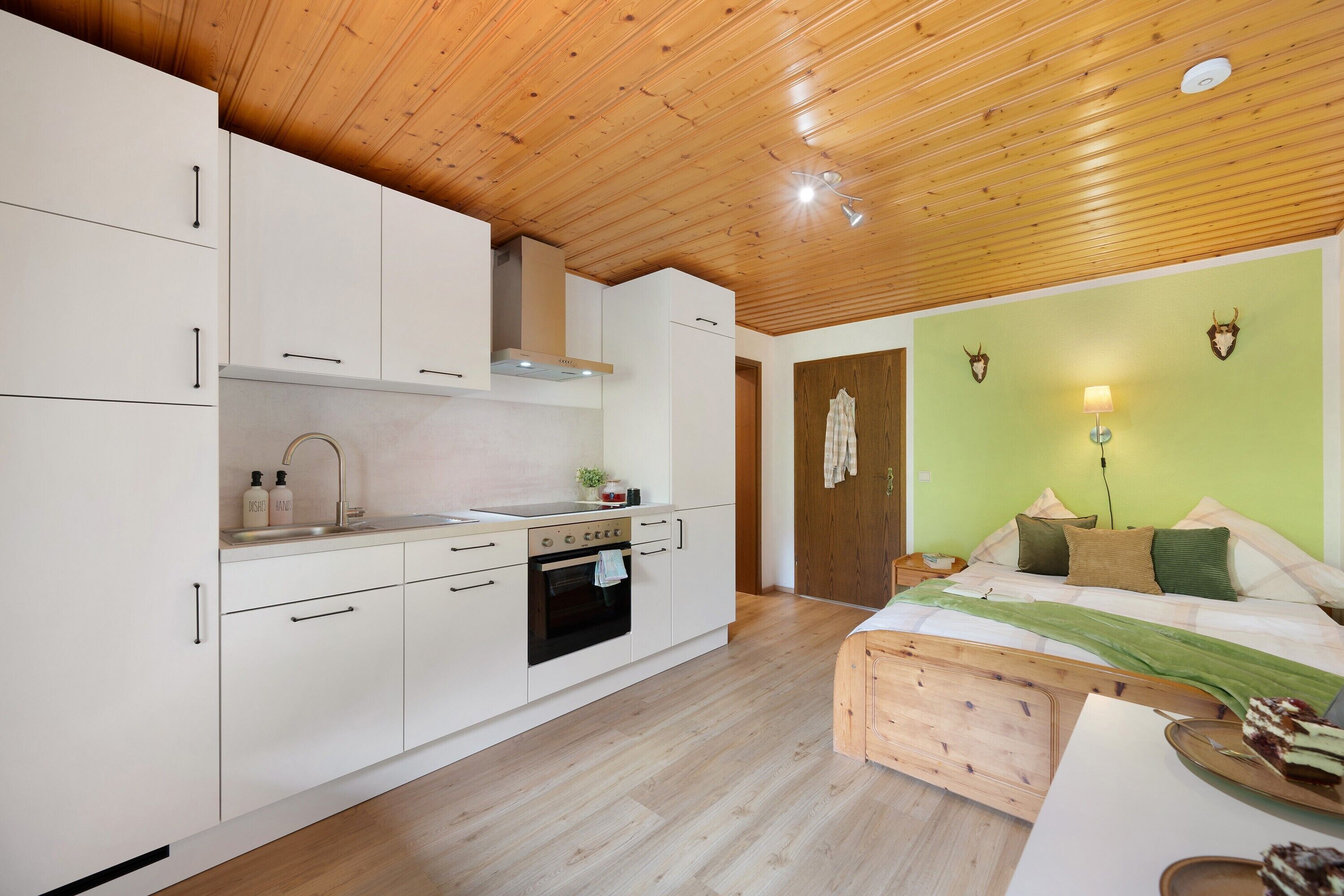 Une cuisine de taille réduite avec des meubles blancs, une cuisinière et un plafond en bois.