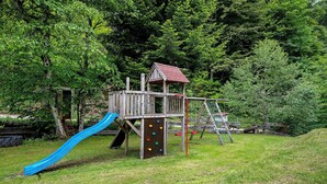 Ein Spielplatz mit Rutsche und Kletterwand, umgeben von Bäumen.