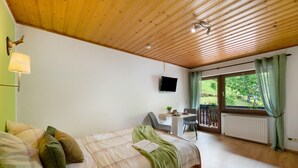 Ein Schlafzimmer mit einem Bett, einem Schreibtisch, einem Stuhl, einem Fernseher und einem Fenster mit Vorhängen.