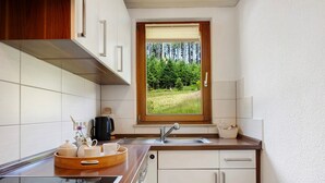 A kitchen with a window view of a forest, a sink, and a wooden tray with kitchen items. - Apartment 'Ringwald' with Mountain View, Shared Garden and Wi-Fi (Biederbach)