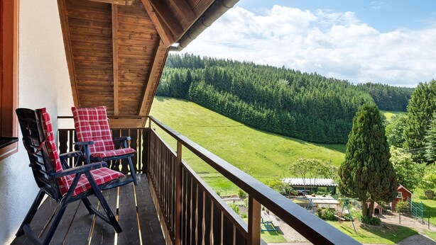 A balcony with two rocking chairs, a wooden ceiling, and a view of a green valley and forest. - Apartment 'Ringwald' with Mountain View, Shared Garden and Wi-Fi (Biederbach)