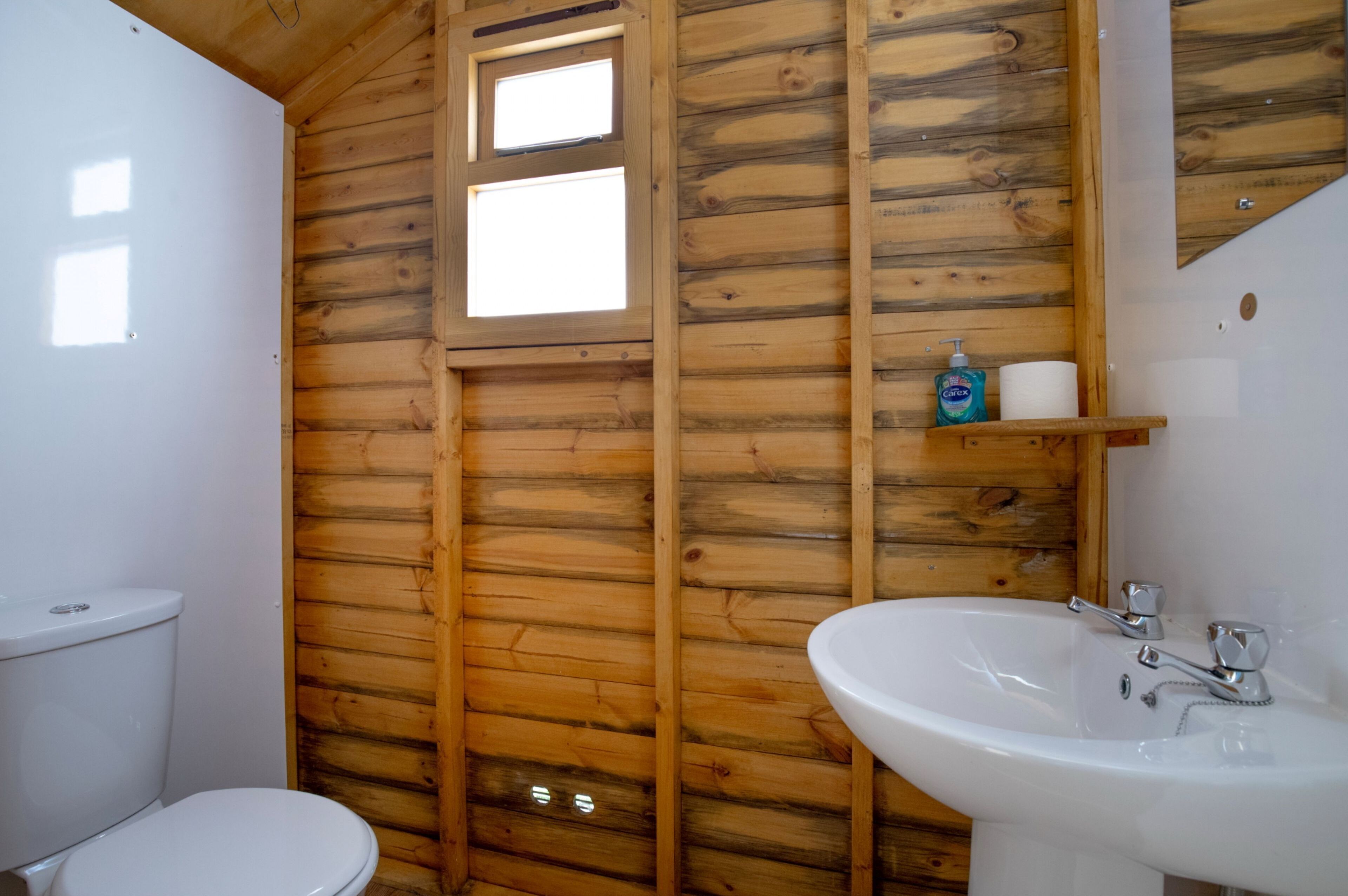 A wooden-paneled bathroom with a toilet, sink, and a small shelf with toiletries.