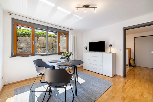 Une cuisine moderne avec une table à manger, des chaises, un téléviseur et une vue sur la verdure environnante.